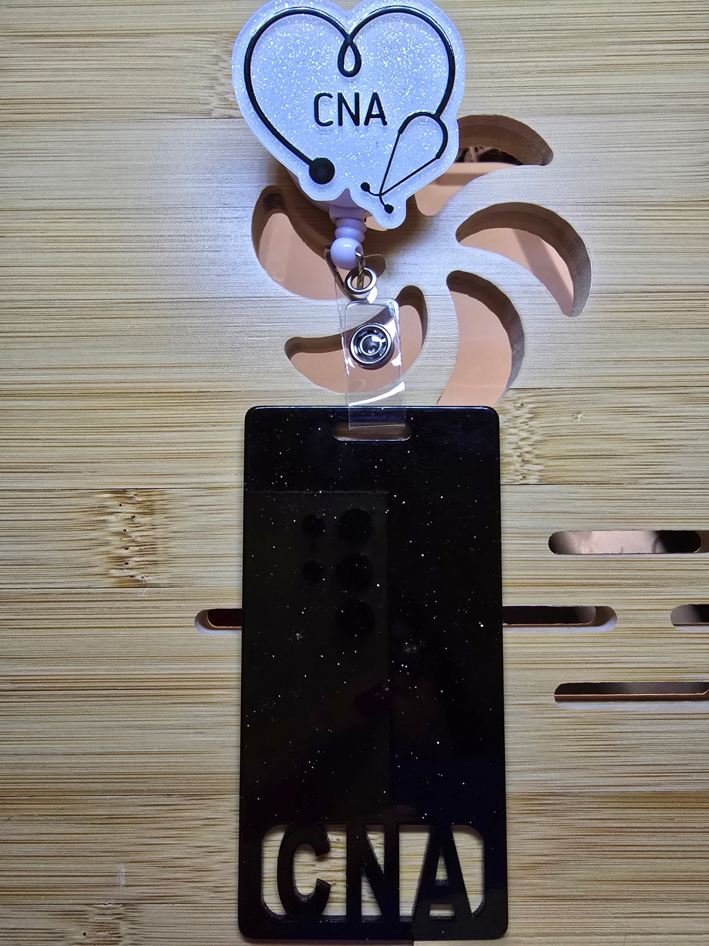 White acrylic flatback with the words CNA in back and a stethoscope in a heart with a black long badge buddy that says CNA