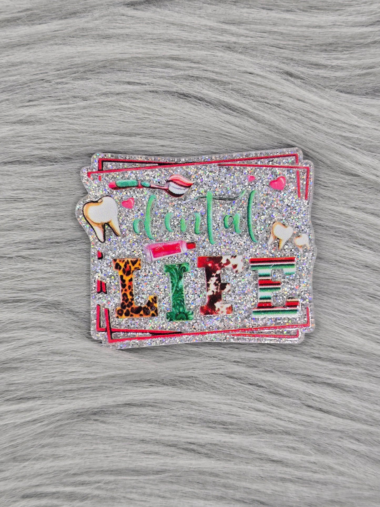 Glitter silver acrylic flatback with the words 'dental life' and pictures of teeth and a tooth brush