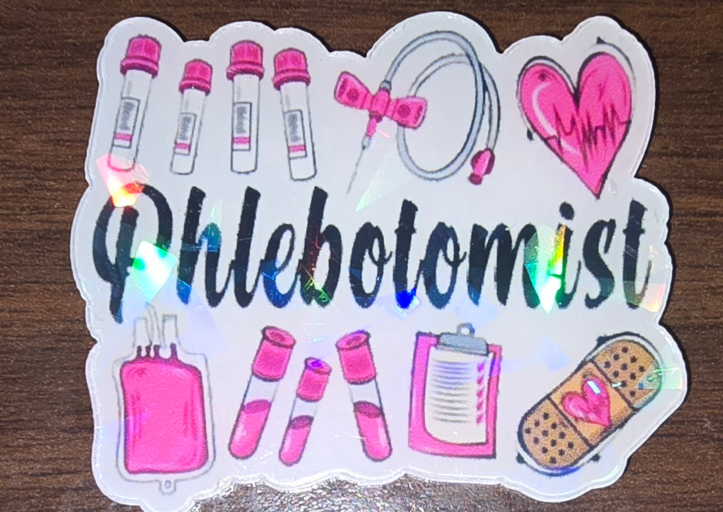Phlebotomist holographic acrylic flatback, pink medical pictures and the word phlebotomist in black in the middle