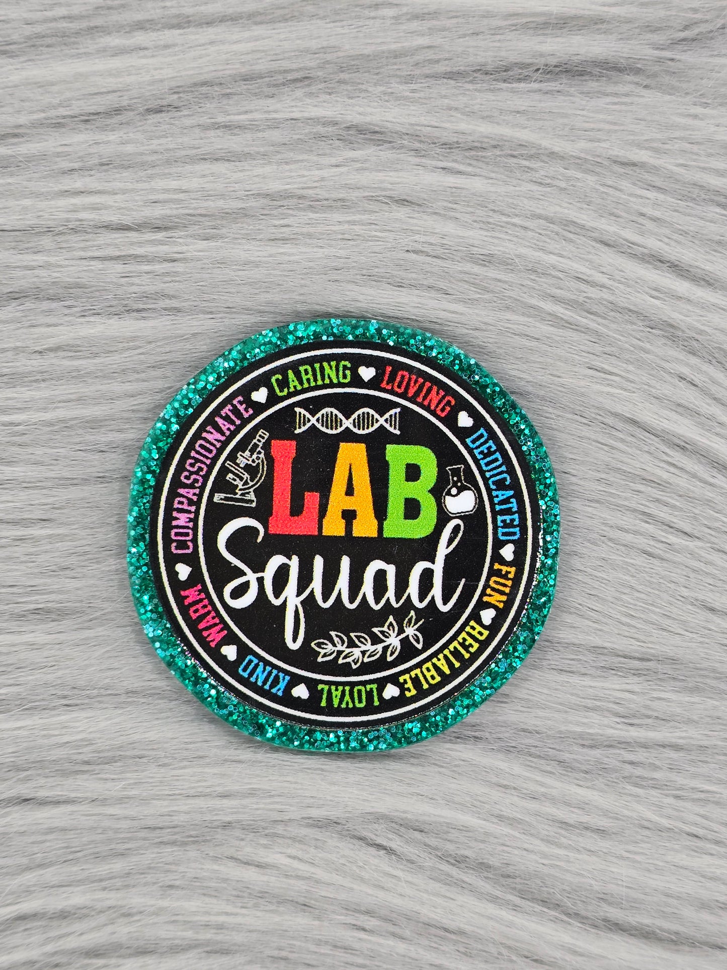 Green Acrylic flatback with a black background with words in the middle that say "LAB Squad" and in a circle around the LAB Squad there are words in rainbow that say "Loving, Dedicated, Fun, Reliable, Loyal, Kind, Warm, Compassionate, Caring"