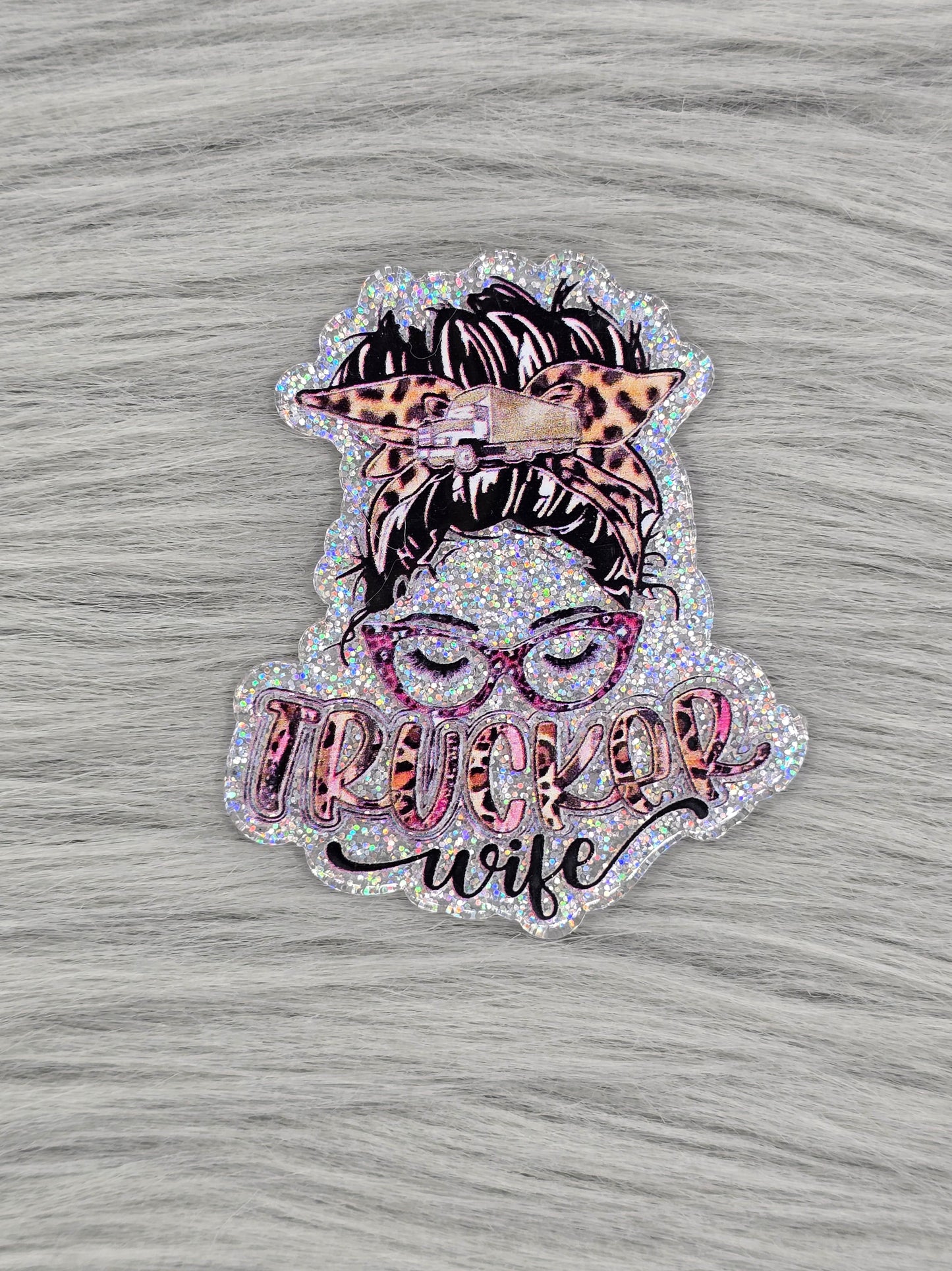 Silver acrylic flatback with a women head with glasses and hair up and the words "Trucker Wife" at the bottom