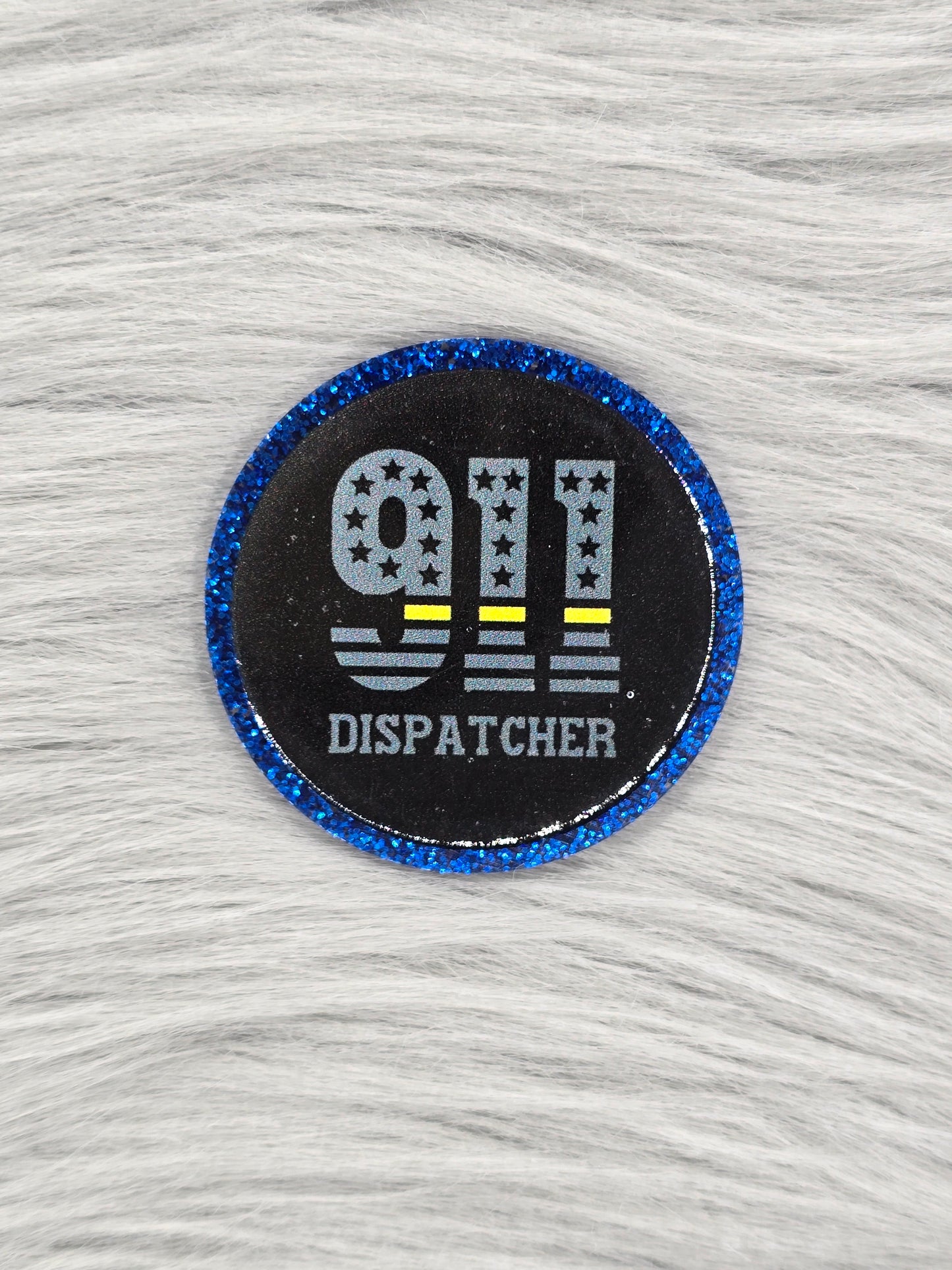 Round acrylic flatback with a glitter blue background, the middle is black and the words/numbers '911 Dispatcher' are in the middle in gray
