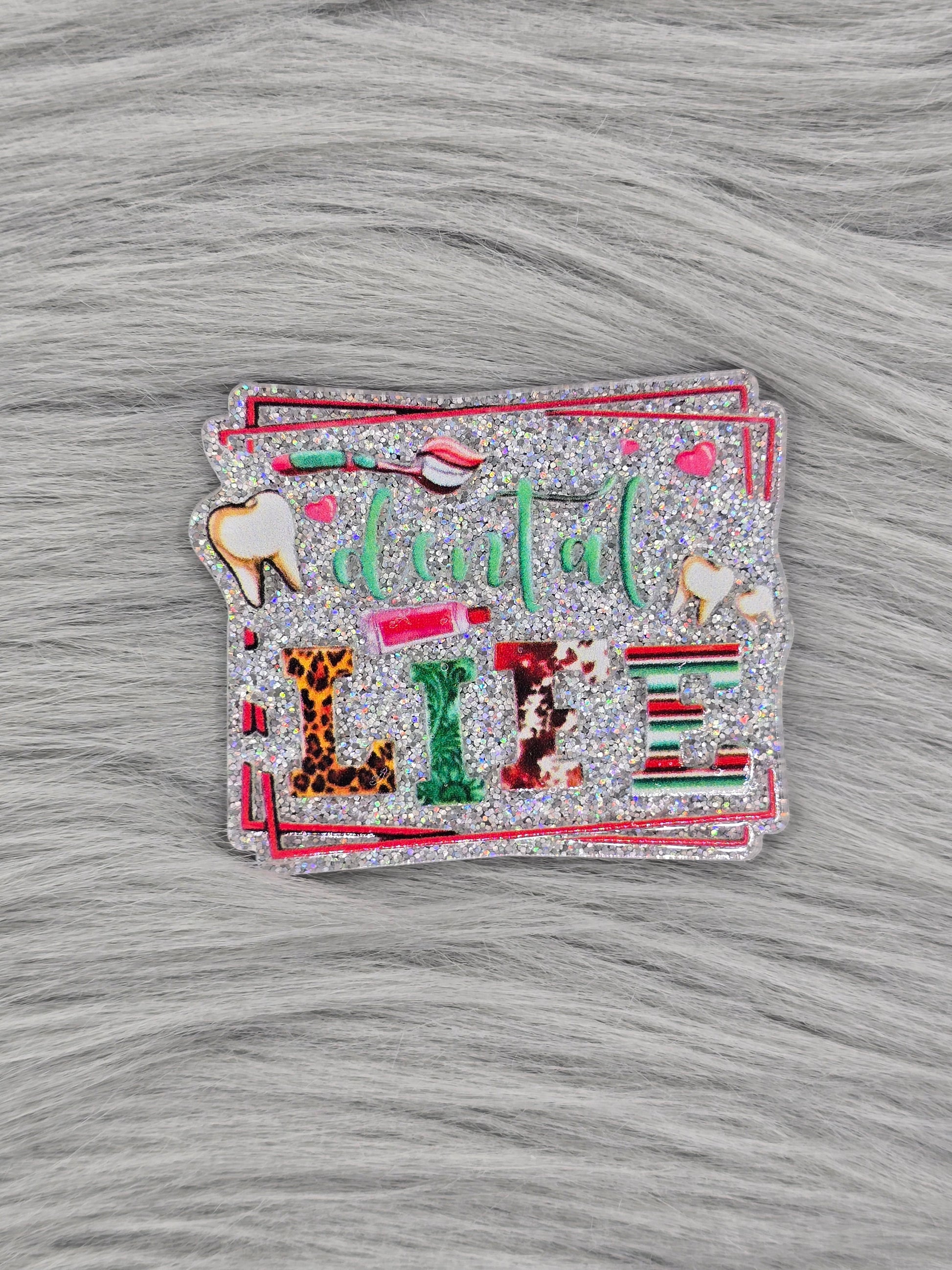 Glitter silver acrylic flatback with the words 'dental life' and pictures of teeth and a tooth brush