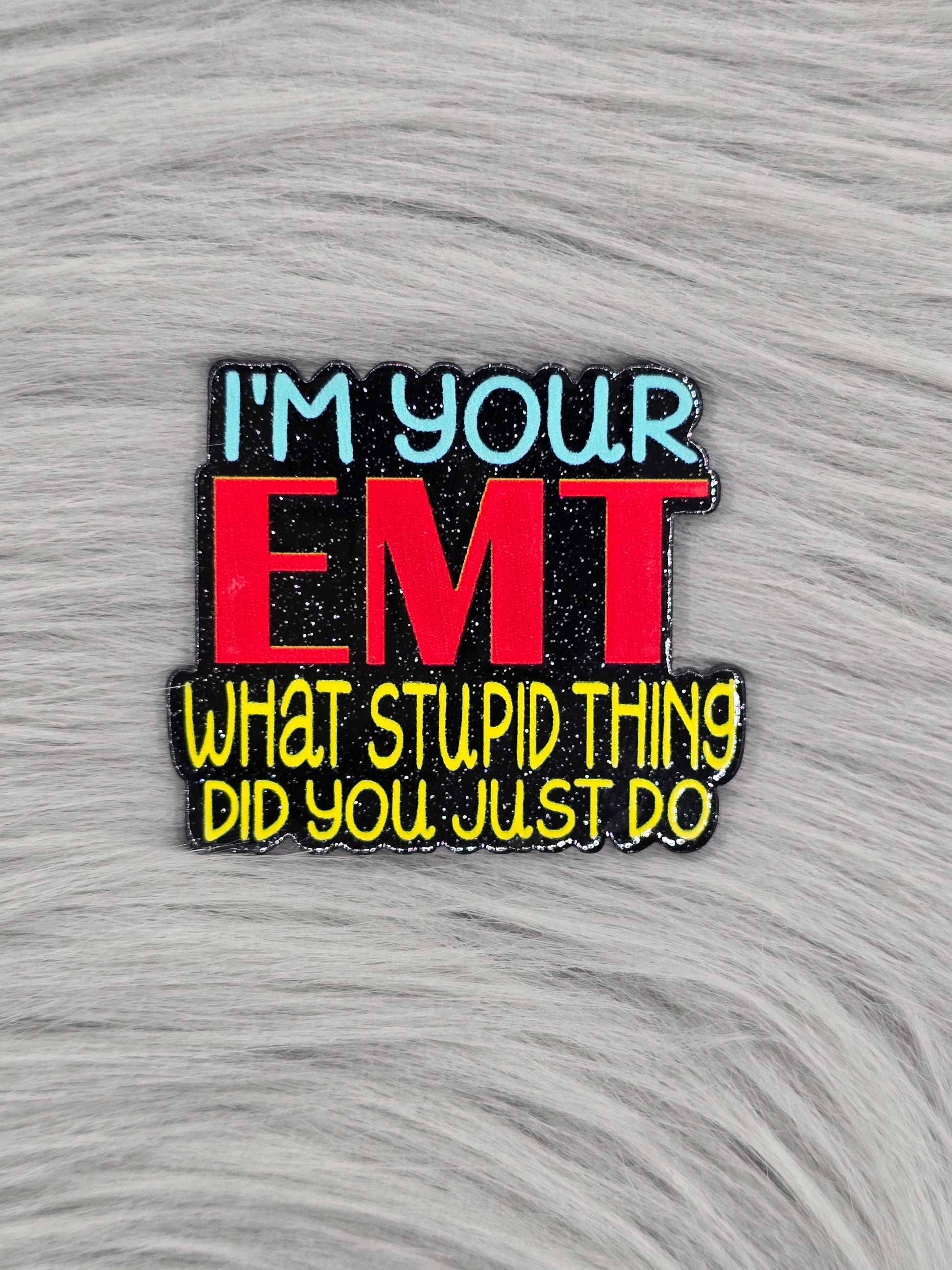 Black glitter acrylic flatback with the words "I'm Your EMT What Stupid Thing Did You Just Do" in blue, red and yellow