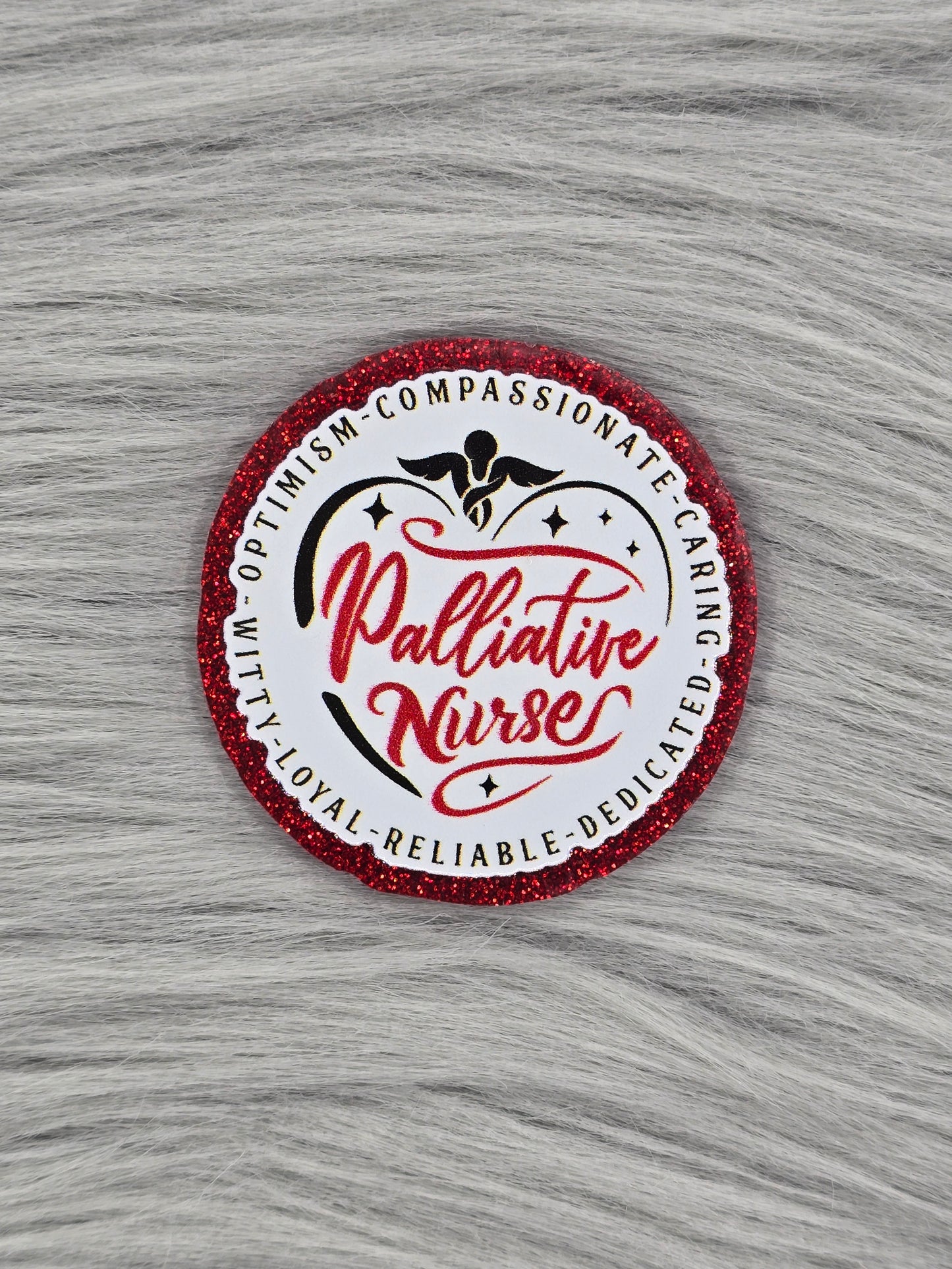 Red glitter flatback with a white background and red words in the middle that say "Palliative Nurse" and on the outside it says" Compassionate, caring, dedicated, reliable, loyal, witty, optimism"