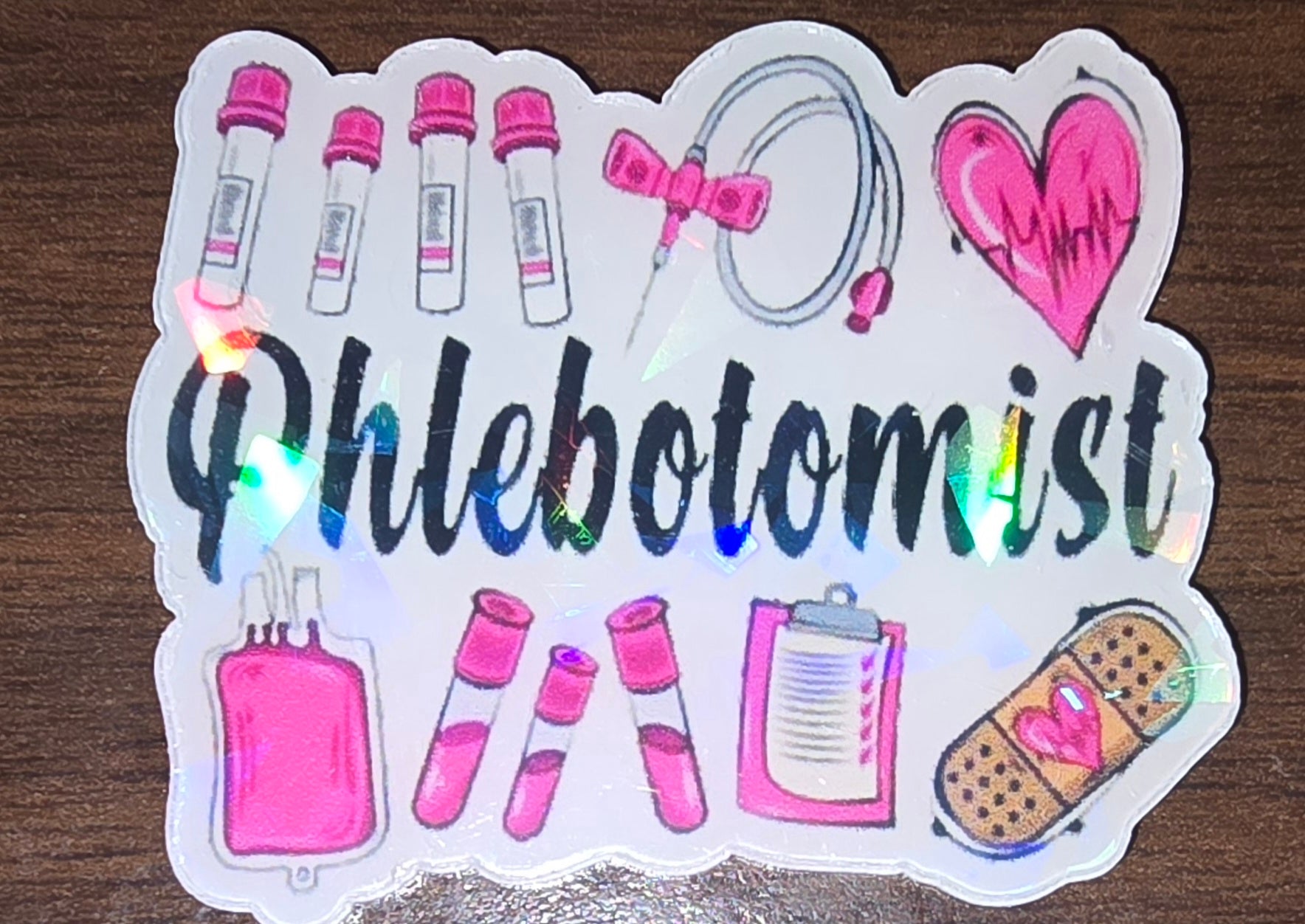 Phlebotomist holographic acrylic flatback, pink medical pictures and the word phlebotomist in black in the middle