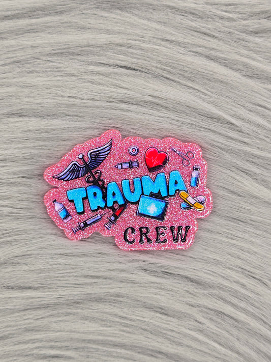 Pink glitter acrylic flatback with the words in blue hat say "trauma crew" with medical pictures