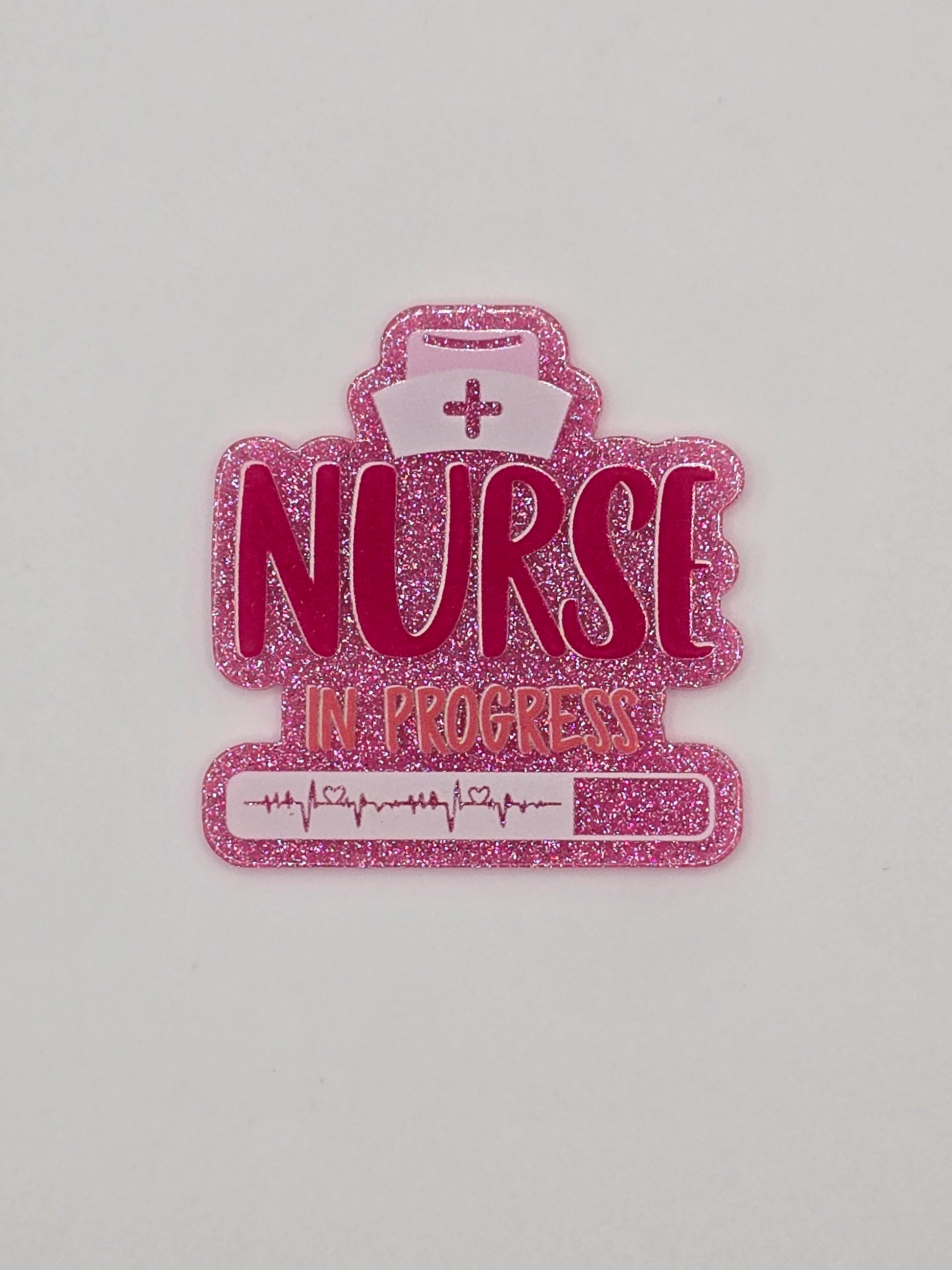 Pink glitter flatback with the words "Nurse In Progress" on it