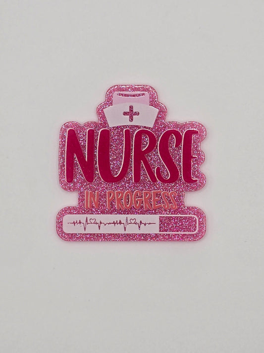 Pink glitter flatback with the words "Nurse In Progress" on it