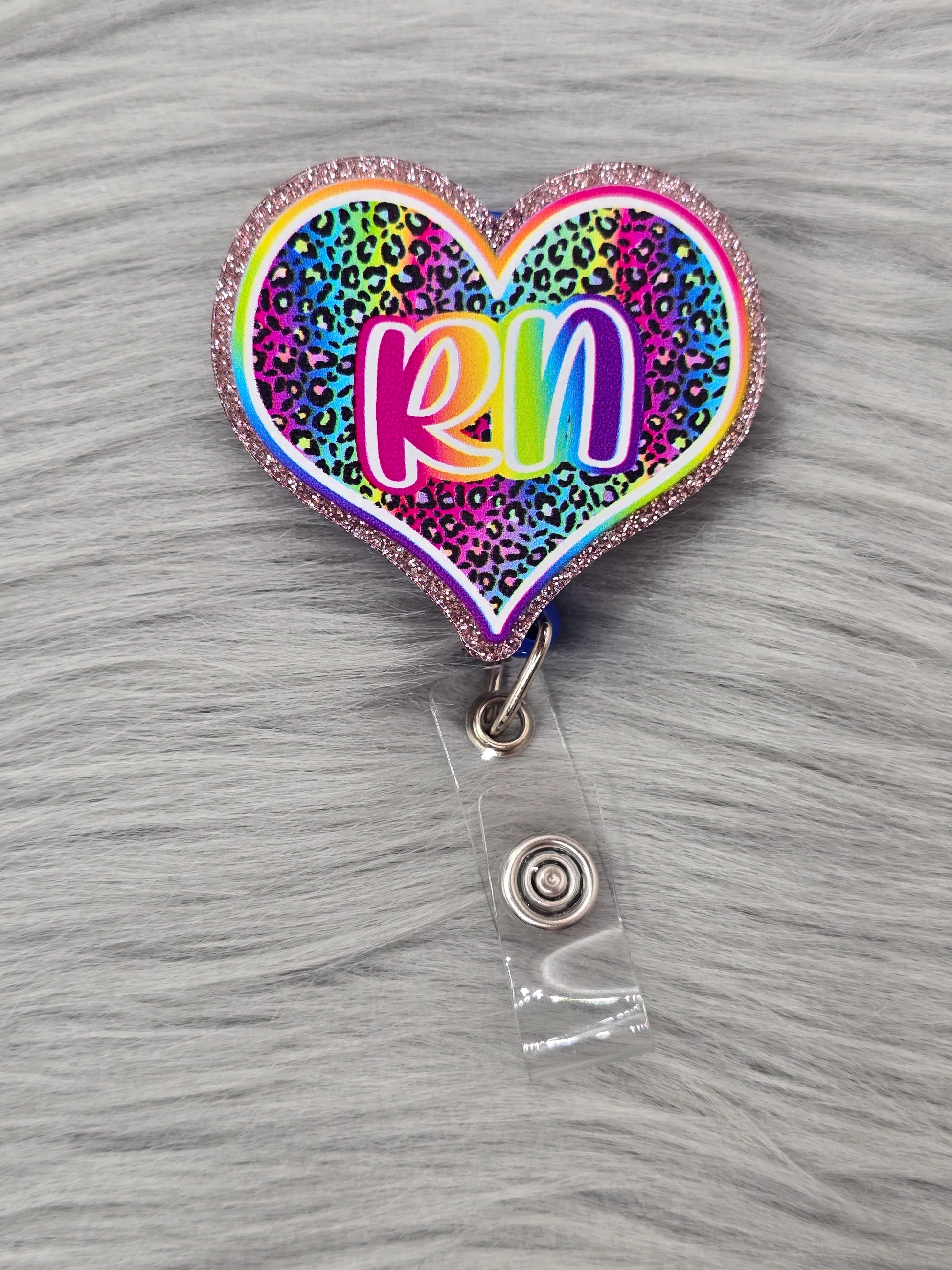 Heart shaped acrylic flatback with a rainbow leopard background and the letters RN in rainbow