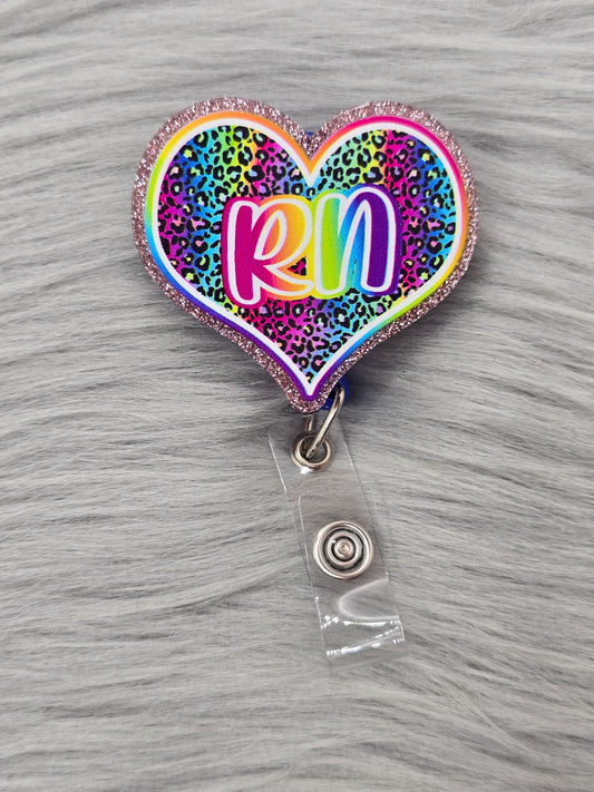Heart shaped acrylic flatback with a rainbow leopard background and the letters RN in rainbow