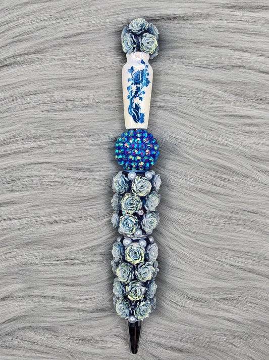 Pen with blue flowers and a white vase with blue flowers and a blue rhinestone bead holding up the vase