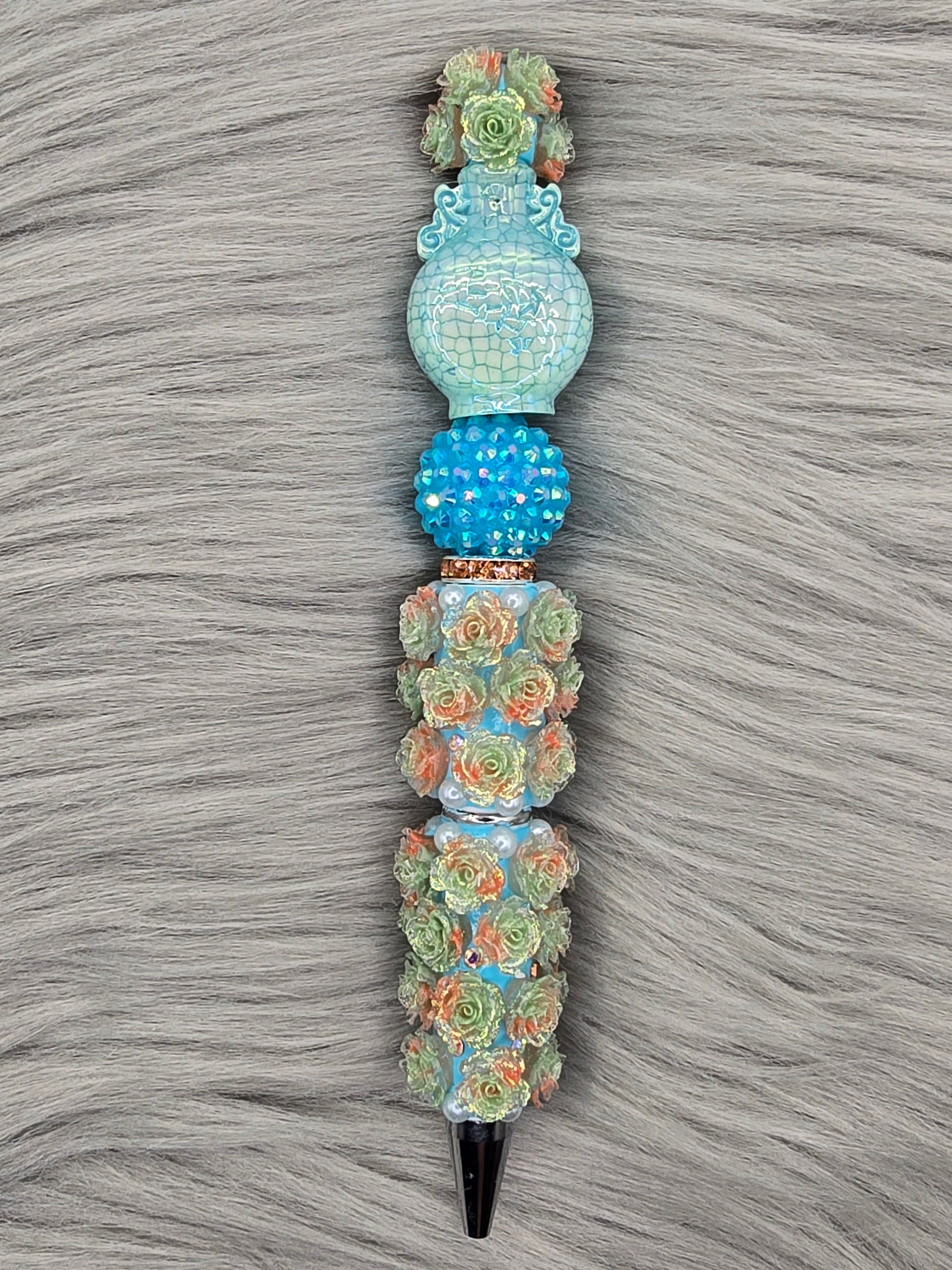 Light blue beadable pen pen with light orange/light green flowers with a blue rhinestone bead, light blue vase at the top
