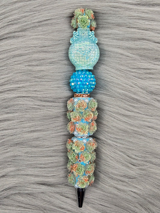 Light blue beadable pen pen with light orange/light green flowers with a blue rhinestone bead, light blue vase at the top