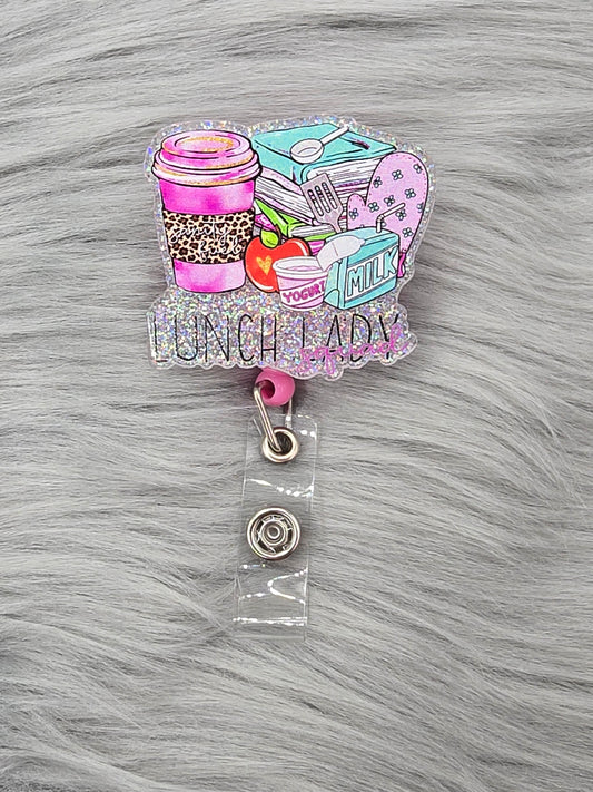 Silver background of an acrylic flatback that says Lunch Lady Squad with lunch items on a pink badge reel