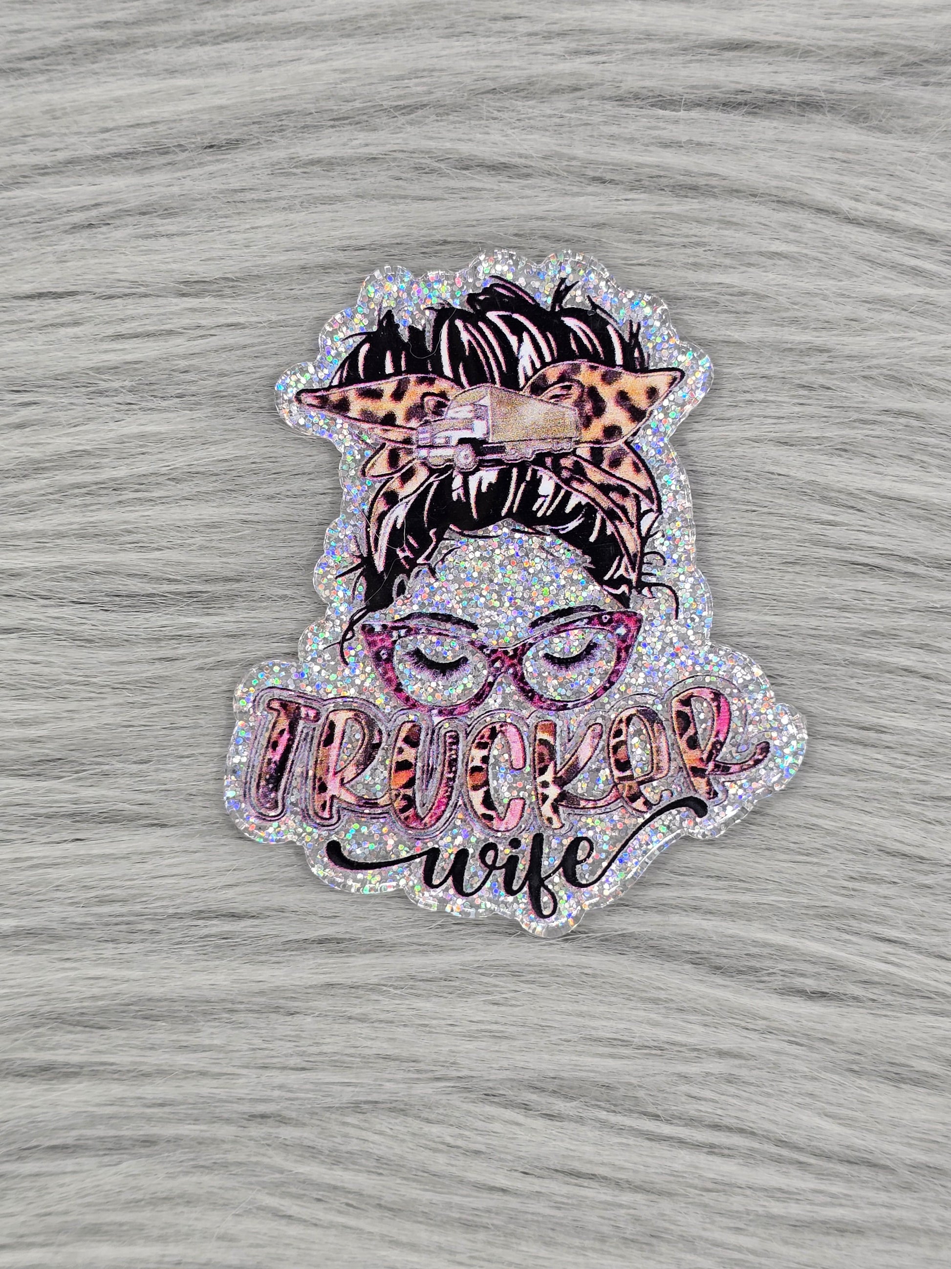Silver acrylic flatback with a women head with glasses and hair up and the words "Trucker Wife" at the bottom