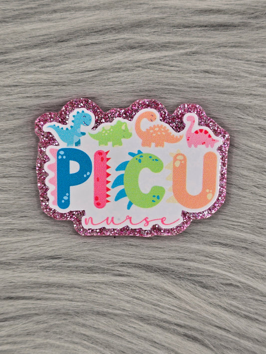 Glitter pink acrylic flatback with the letters "PICU nurse" with rainbow dinosaurs at the top