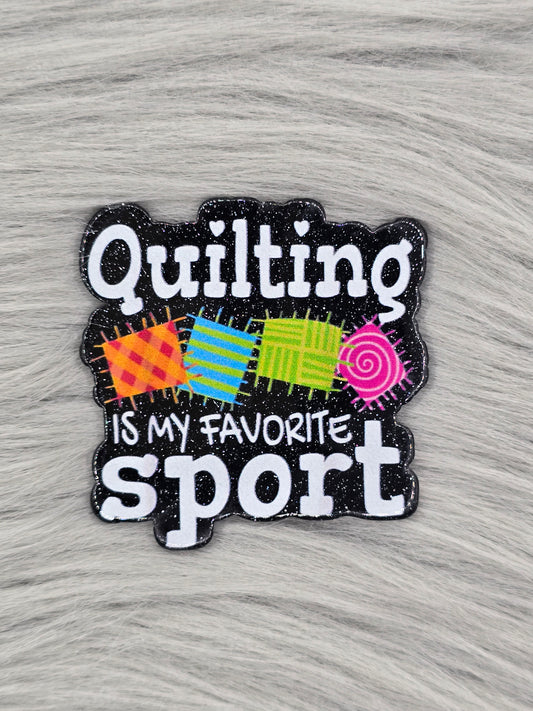 Black glitter acrylic flatback with white words saying "Quilting is my favorite sport" and 4 colorful quilts in the middle