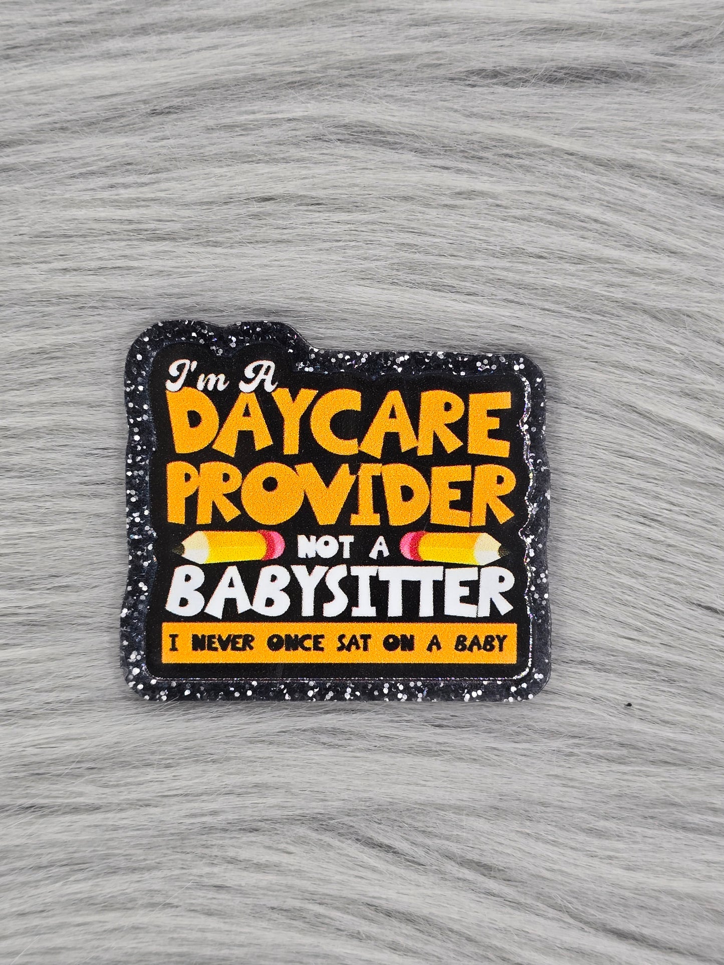 Black acrylic flatback with the words in yellow and white that say " I'm a daycare provider not a babysitter I never once sat on a baby"