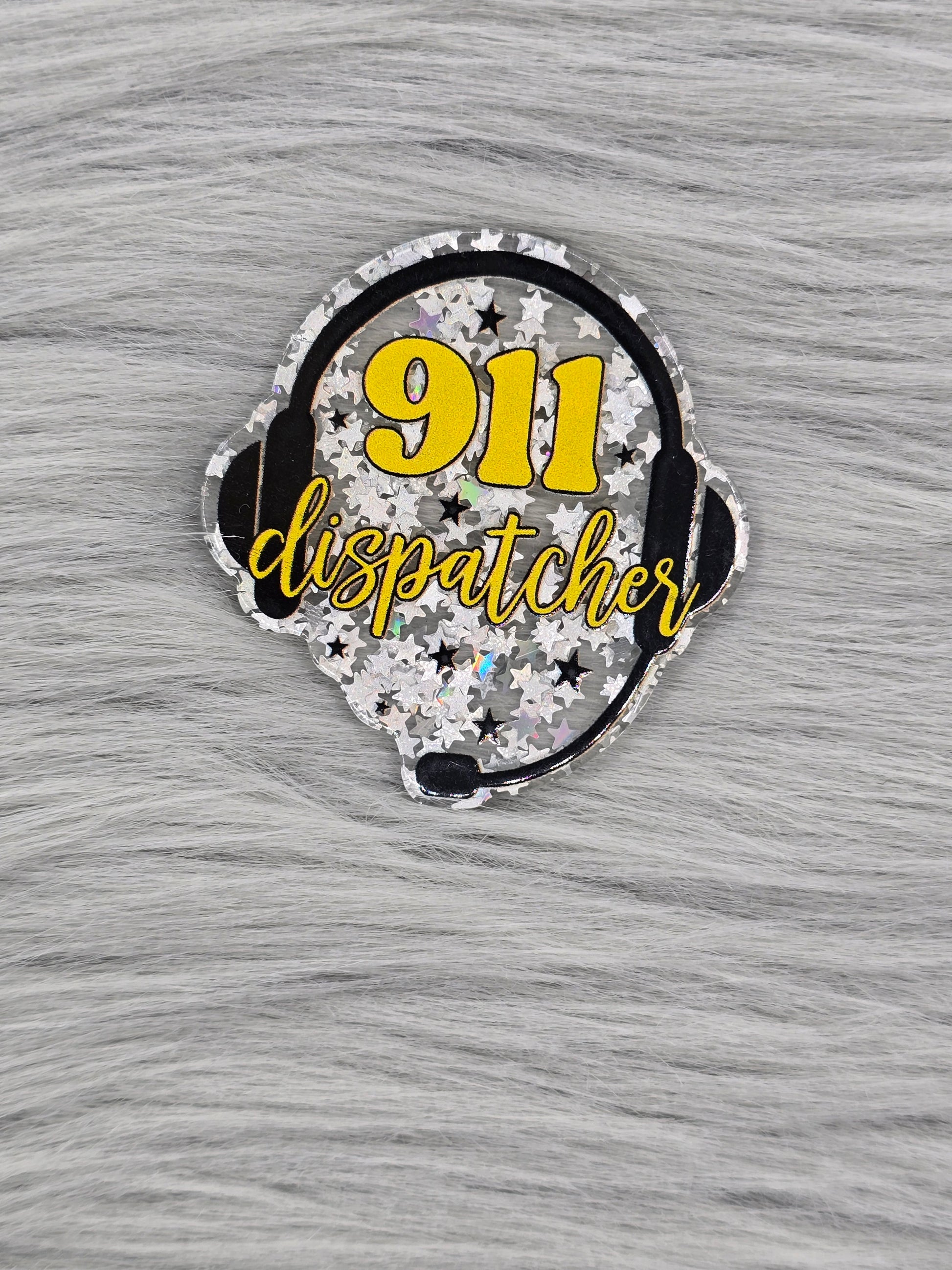 Glitter silver acrylic flatback with the number 911 and the word dispatcher in yellow with a head set