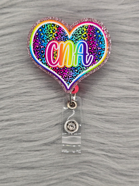 Heart shaped acrylic flatback with a rainbow leopard background and the letters CNA in rainbow