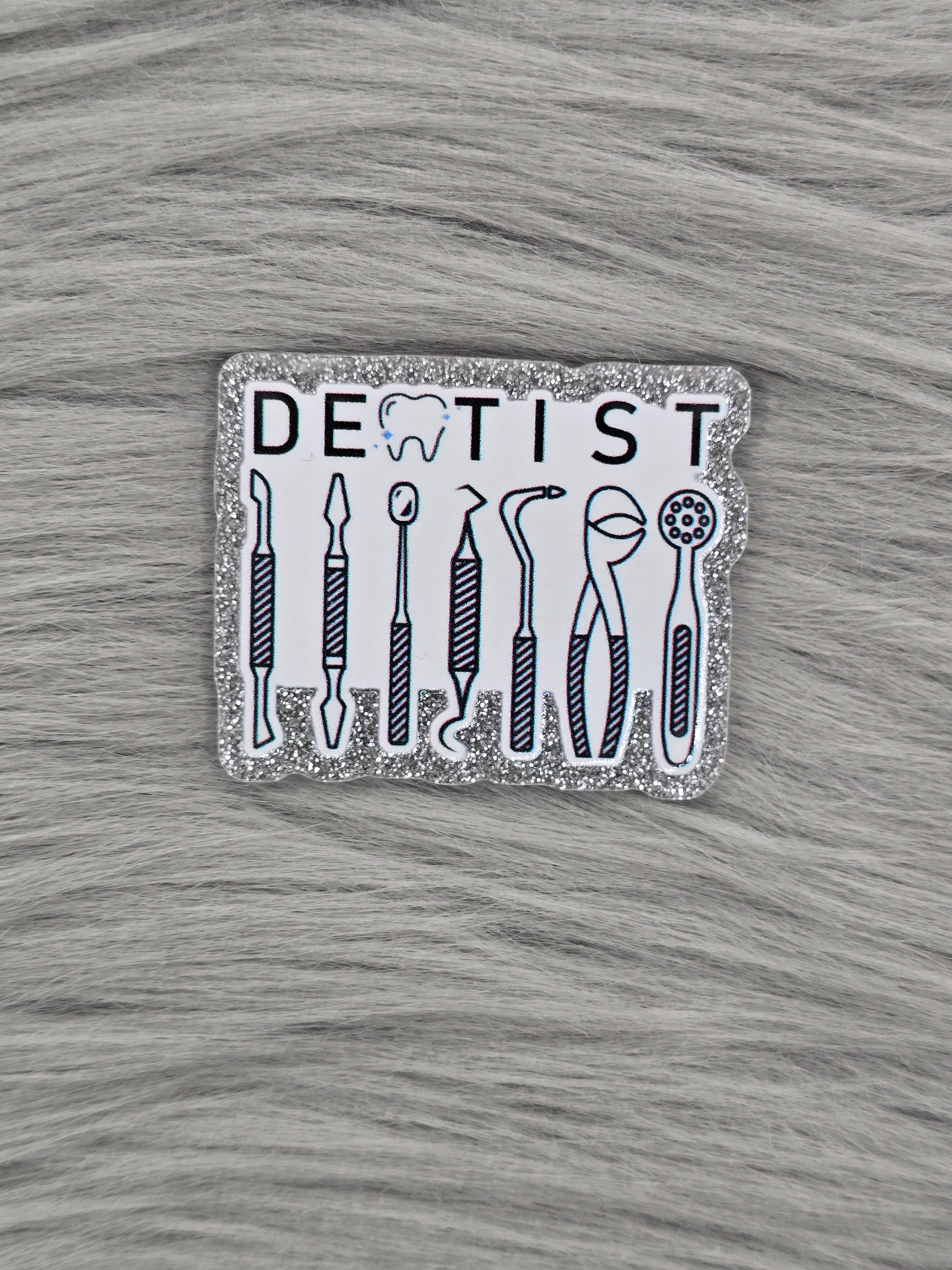 Glitter silver acrylic flatback with a white background and the word Dentist at the top in back and dental equipment under.